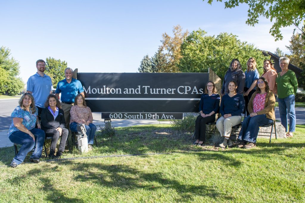 The Moulton and Turner CPAs team standing and seated beside the firm's sign at 600 South 19th Ave.